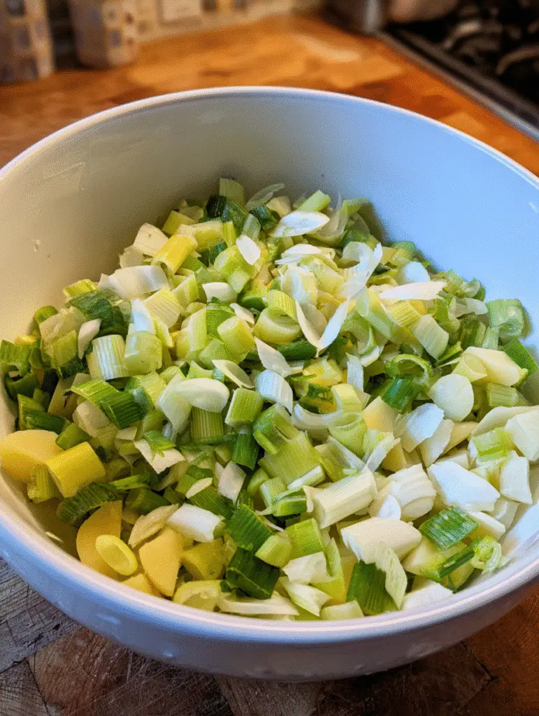 Leek and potato soup preparation with chopped leeks and sliced potatoes in a white mixing bowl.