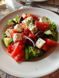 Greek salad recipe with feta cheese, tomatoes, cucumbers, olives, and red onions in a white bowl.