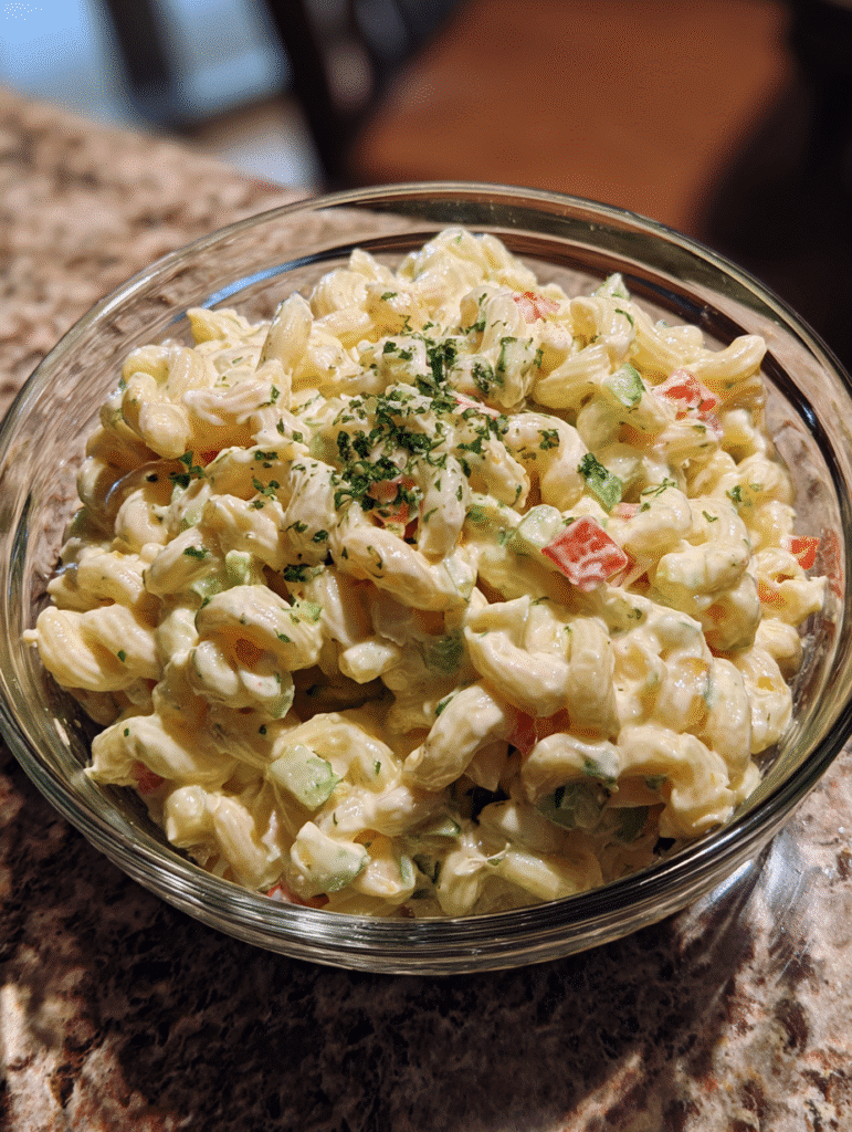 Macaroni salad recipe with creamy dressing, diced vegetables, and fresh parsley in a glass bowl.
